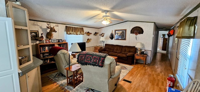 living room featuring ceiling fan, hardwood / wood-style floors, vaulted ceiling, and a textured ceiling