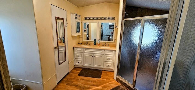 bathroom with a textured ceiling, vaulted ceiling, dual vanity, and hardwood / wood-style flooring