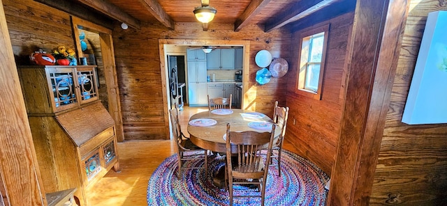 dining area featuring beam ceiling, wooden walls, ceiling fan, and light wood-type flooring