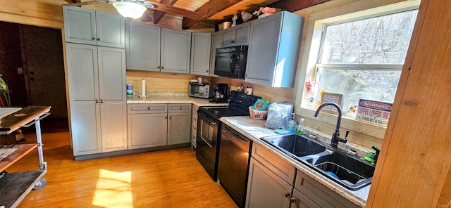 kitchen with gray cabinetry, black appliances, sink, light hardwood / wood-style flooring, and beam ceiling