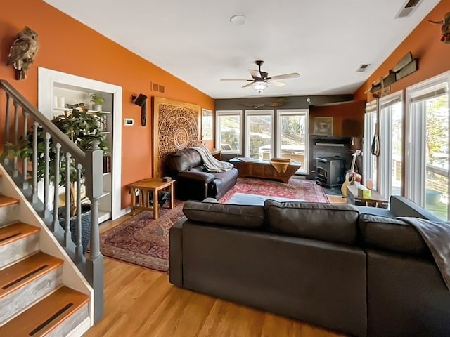 living room with light hardwood / wood-style floors, ceiling fan, a wood stove, and lofted ceiling