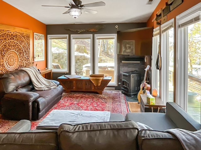 living room featuring plenty of natural light, ceiling fan, vaulted ceiling, and a wood stove