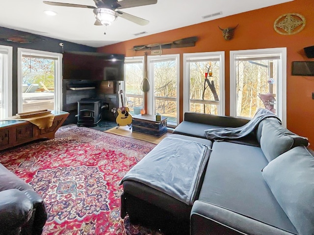 living room with wood-type flooring, ceiling fan, and a wood stove