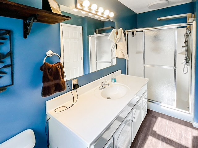 bathroom featuring a shower with door, toilet, vanity with extensive cabinet space, and hardwood / wood-style flooring