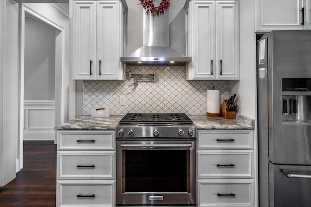 kitchen with appliances with stainless steel finishes, wall chimney range hood, light stone counters, dark wood-type flooring, and white cabinets