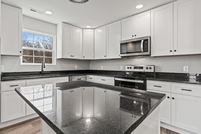 kitchen featuring stainless steel appliances, dark stone countertops, light hardwood / wood-style floors, and white cabinets