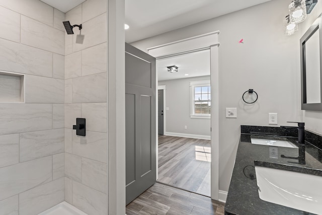 bathroom with double sink, a tile shower, hardwood / wood-style floors, and vanity with extensive cabinet space