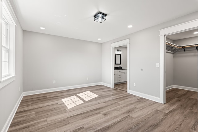 unfurnished bedroom featuring a closet, a walk in closet, ensuite bathroom, and light wood-type flooring