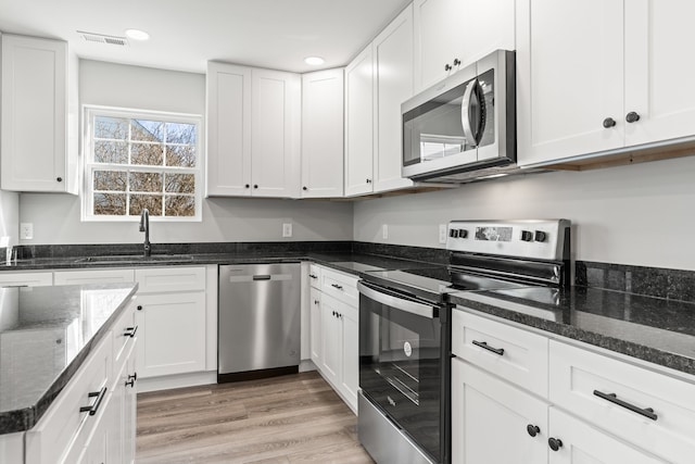 kitchen featuring sink, white cabinets, appliances with stainless steel finishes, dark stone countertops, and light wood-type flooring