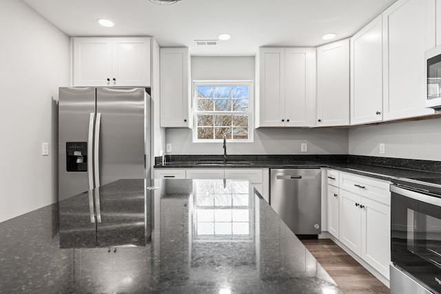 kitchen featuring white cabinetry, appliances with stainless steel finishes, sink, dark stone countertops, and dark hardwood / wood-style flooring