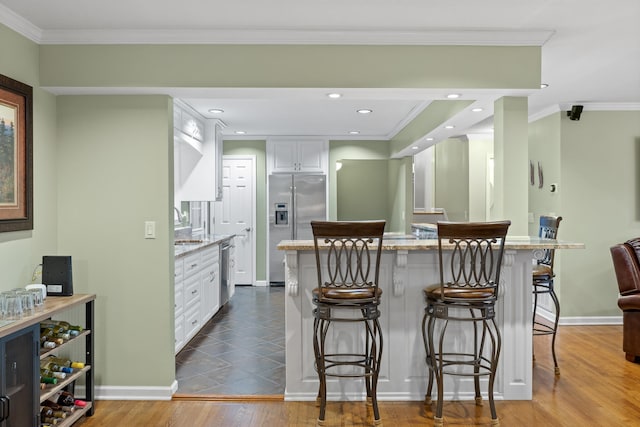 kitchen featuring a kitchen breakfast bar, white cabinetry, light stone counters, stainless steel appliances, and hardwood / wood-style flooring