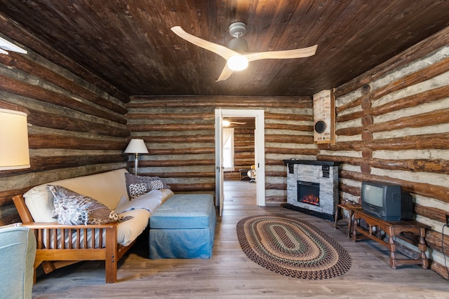 sitting room featuring wood-type flooring, rustic walls, wooden ceiling, a stone fireplace, and ceiling fan