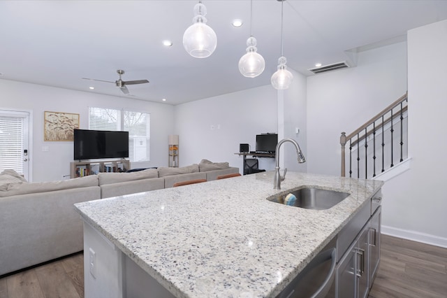 kitchen with an island with sink, decorative light fixtures, dark wood-type flooring, sink, and light stone counters