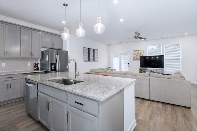 kitchen with appliances with stainless steel finishes, a center island with sink, light wood-type flooring, ceiling fan, and sink