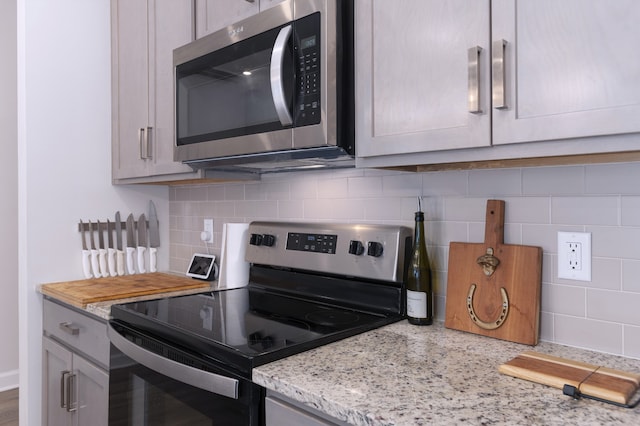 kitchen with appliances with stainless steel finishes, tasteful backsplash, and light stone counters