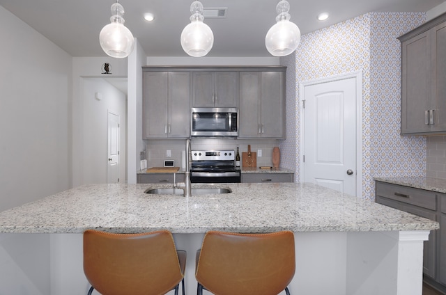 kitchen featuring stainless steel appliances, backsplash, a center island with sink, and decorative light fixtures