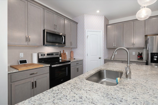 kitchen featuring stainless steel appliances, light stone countertops, backsplash, hanging light fixtures, and sink