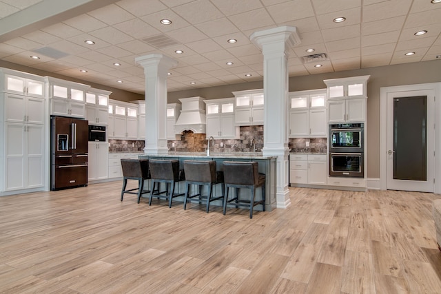 kitchen with custom range hood, a breakfast bar area, stainless steel double oven, white cabinetry, and high end fridge