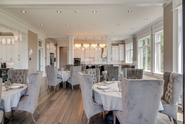 dining space with a notable chandelier, crown molding, ornate columns, and wood-type flooring