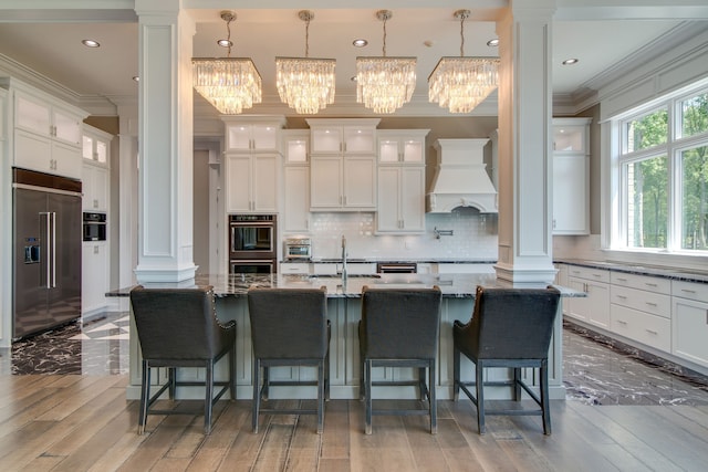 kitchen featuring appliances with stainless steel finishes, tasteful backsplash, a breakfast bar, premium range hood, and a chandelier