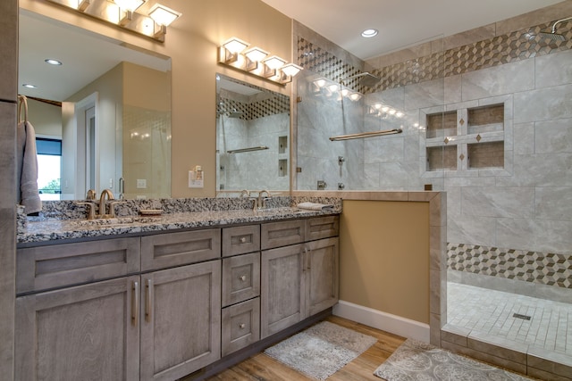 bathroom featuring dual vanity, wood-type flooring, and tiled shower