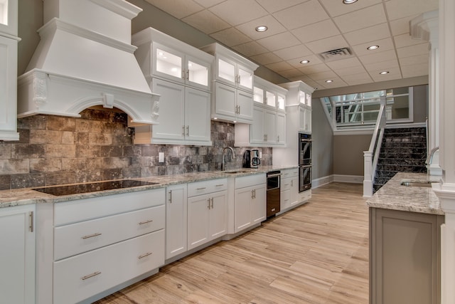 kitchen with white cabinets, sink, custom range hood, and tasteful backsplash