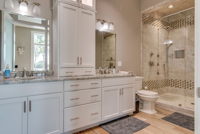 bathroom with double sink, large vanity, toilet, hardwood / wood-style flooring, and a tile shower