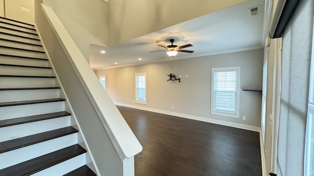 stairway featuring plenty of natural light, crown molding, ceiling fan, and dark wood-type flooring