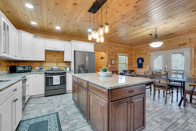 kitchen with hanging light fixtures, stainless steel appliances, white cabinets, wood walls, and french doors