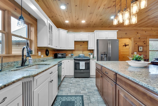 kitchen with hanging light fixtures, sink, stainless steel appliances, white cabinets, and wood walls