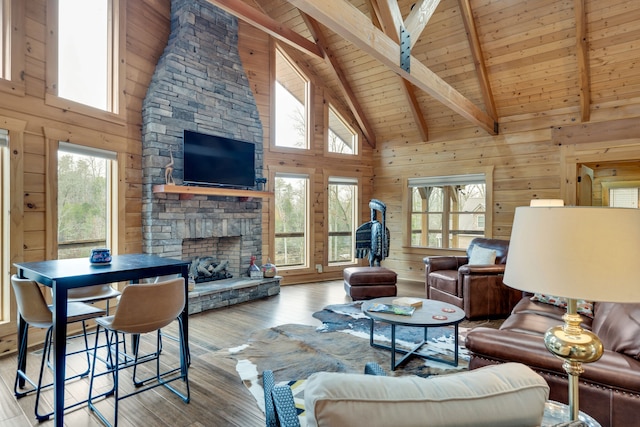 living room with wooden ceiling, wood walls, high vaulted ceiling, a stone fireplace, and light wood-type flooring