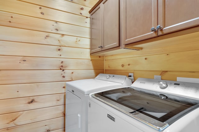 laundry room featuring wooden walls, cabinets, and washing machine and clothes dryer