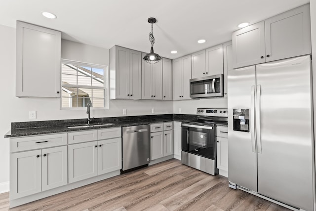 kitchen with sink, hanging light fixtures, dark stone countertops, light hardwood / wood-style floors, and stainless steel appliances