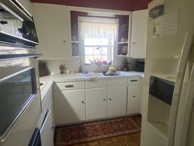 kitchen featuring sink, dark parquet flooring, white cabinetry, and stainless steel oven