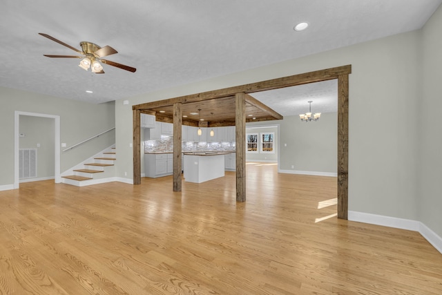 unfurnished living room with light wood-type flooring and ceiling fan with notable chandelier