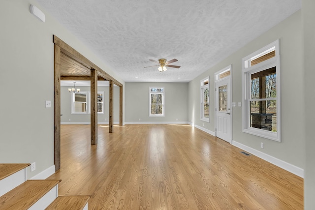 empty room with light hardwood / wood-style flooring, a textured ceiling, and ceiling fan with notable chandelier