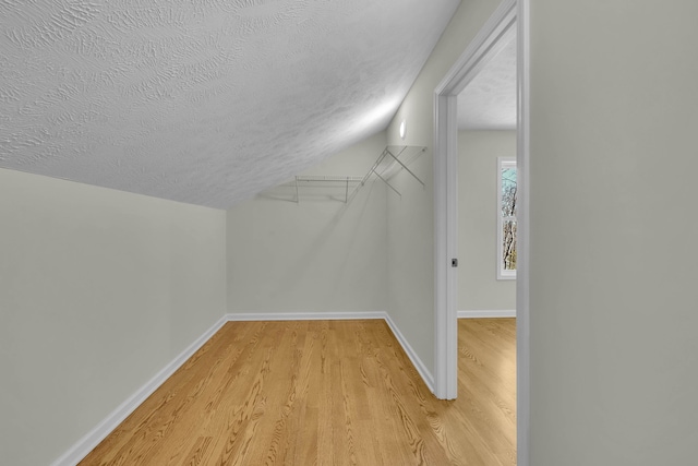 bonus room with a textured ceiling, light hardwood / wood-style floors, and vaulted ceiling