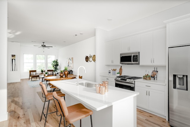 kitchen with ceiling fan, appliances with stainless steel finishes, light hardwood / wood-style floors, sink, and an island with sink