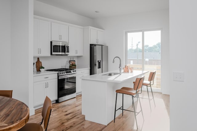 kitchen featuring stainless steel appliances, light hardwood / wood-style floors, sink, a center island with sink, and white cabinets