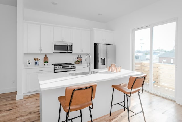 kitchen featuring a center island with sink, stainless steel appliances, light wood-type flooring, sink, and a kitchen breakfast bar