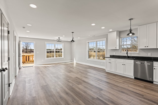 kitchen featuring stainless steel dishwasher, white cabinets, hanging light fixtures, light wood-type flooring, and sink