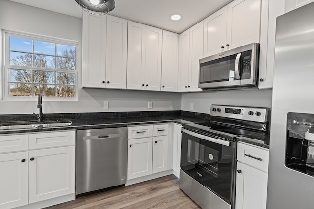 kitchen with sink, dark stone counters, white cabinets, light hardwood / wood-style floors, and stainless steel appliances