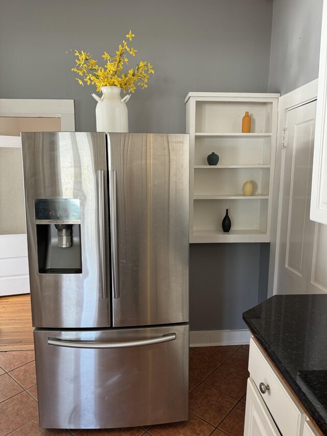 kitchen with dark stone counters, white cabinetry, dark tile patterned flooring, and stainless steel refrigerator with ice dispenser