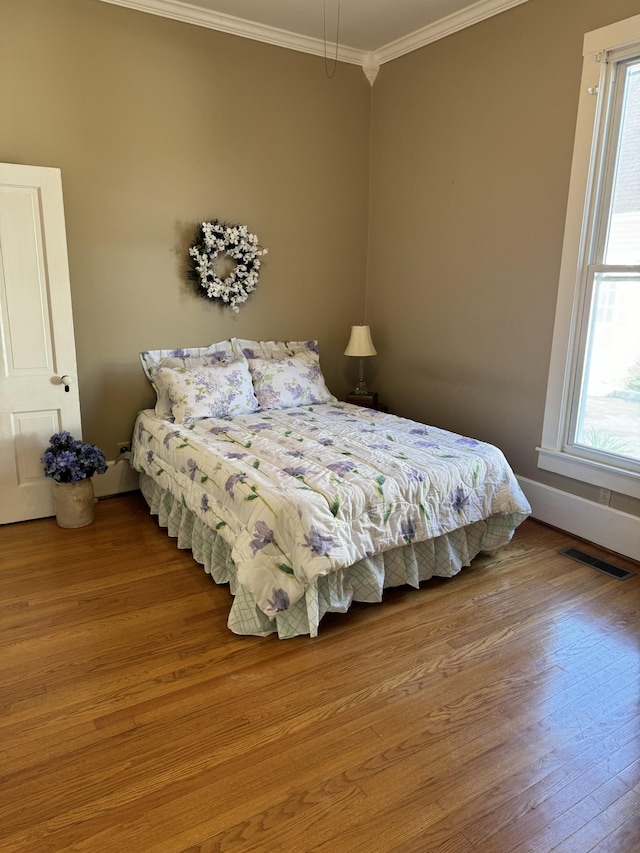 bedroom with wood-type flooring, crown molding, and multiple windows