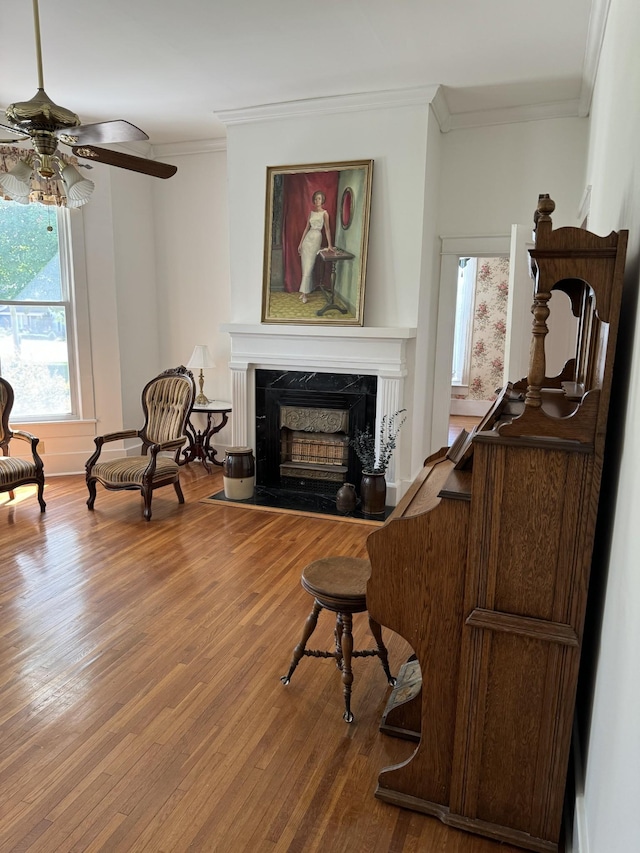 living area with a high end fireplace, hardwood / wood-style flooring, ceiling fan, and crown molding