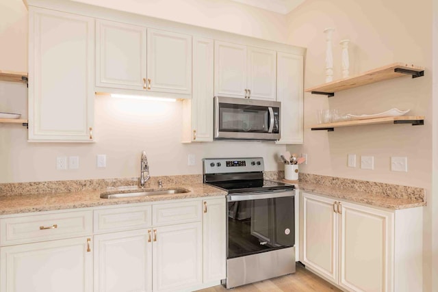 kitchen with white cabinets, sink, stainless steel appliances, light stone countertops, and light hardwood / wood-style floors