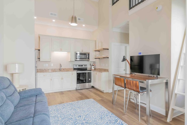 kitchen featuring pendant lighting, sink, white cabinetry, a towering ceiling, and appliances with stainless steel finishes