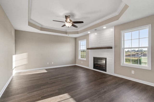 unfurnished living room with dark wood-type flooring, a raised ceiling, ceiling fan, ornamental molding, and a large fireplace