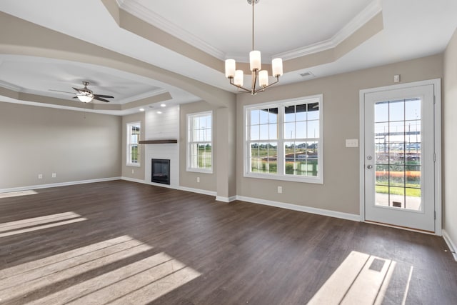 unfurnished living room featuring a large fireplace, dark hardwood / wood-style flooring, a tray ceiling, ceiling fan with notable chandelier, and ornamental molding