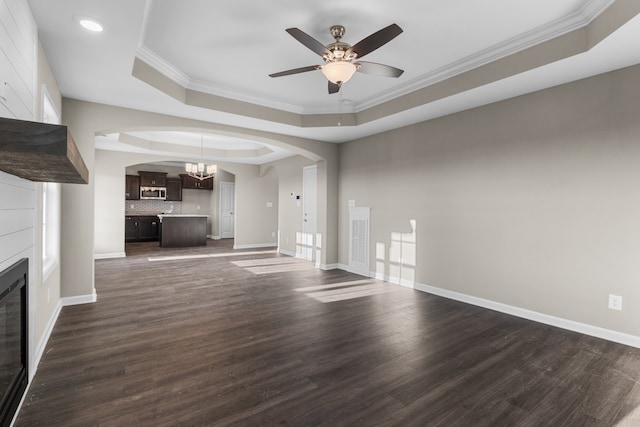 unfurnished living room with ceiling fan with notable chandelier, dark hardwood / wood-style floors, a raised ceiling, and ornamental molding